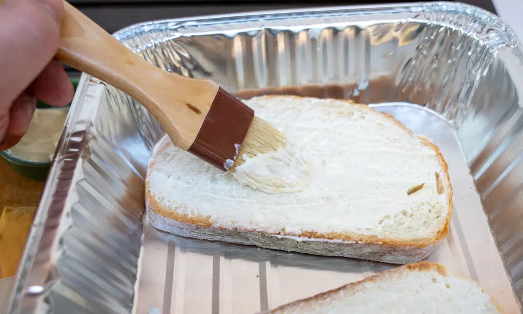 brushing mayo on bread to make a grilled cheese sandwich 
