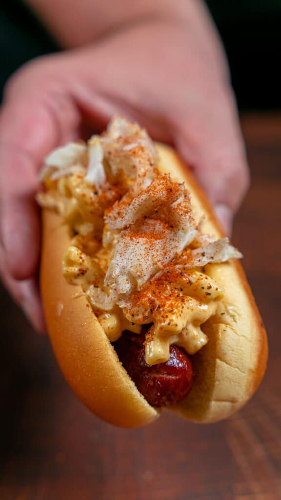 holding a crab Mac and cheese hot dog topped with old bay