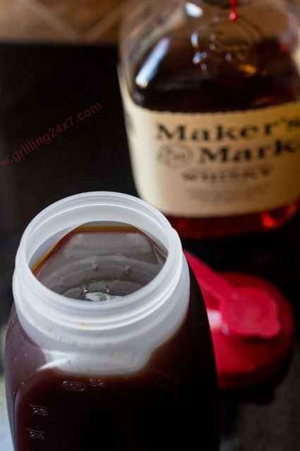 Sweet Whiskey BBQ Sauce in clear bottle with whiskey bottle in the background 