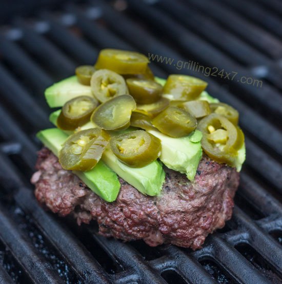 Burger with avocado and jalapeno peppers sitting on the grill - grilling24x7.com