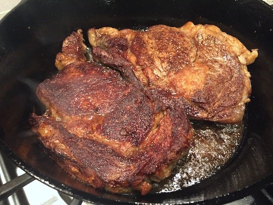 Cooking steaks in a greasy cast iron skillet.