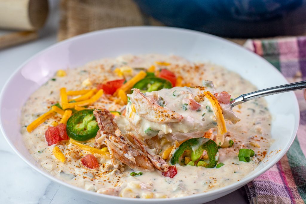 Bowl of creamy white crab chili topped with cheese, corn, jalapeño and tomato