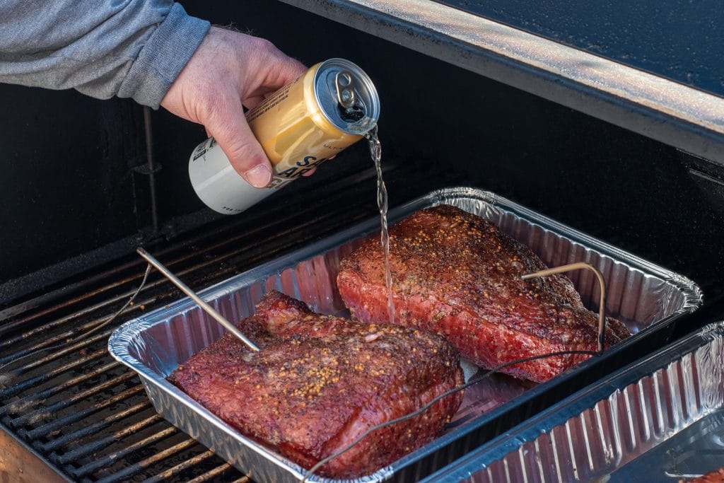 pouring saint archer gold low carb beer into a pan with smoked corned beef