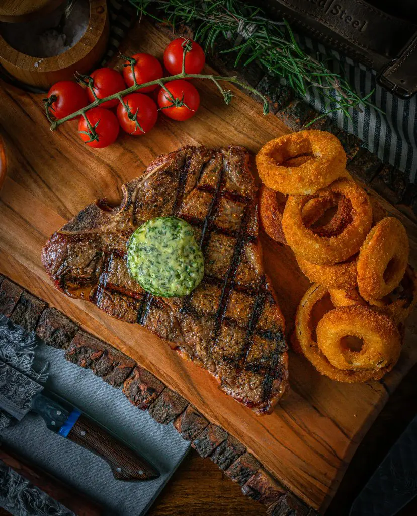 Grilled t bone steak using a charcoal grill with onion rings on the side