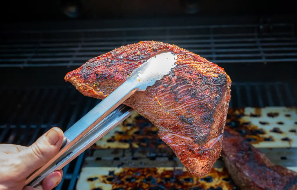 Whole Tri Tip held by tongs over the grill