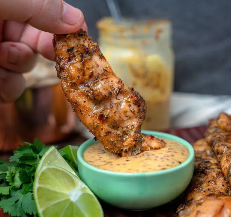 dipping jerk chicken tender into honey dijon dressing