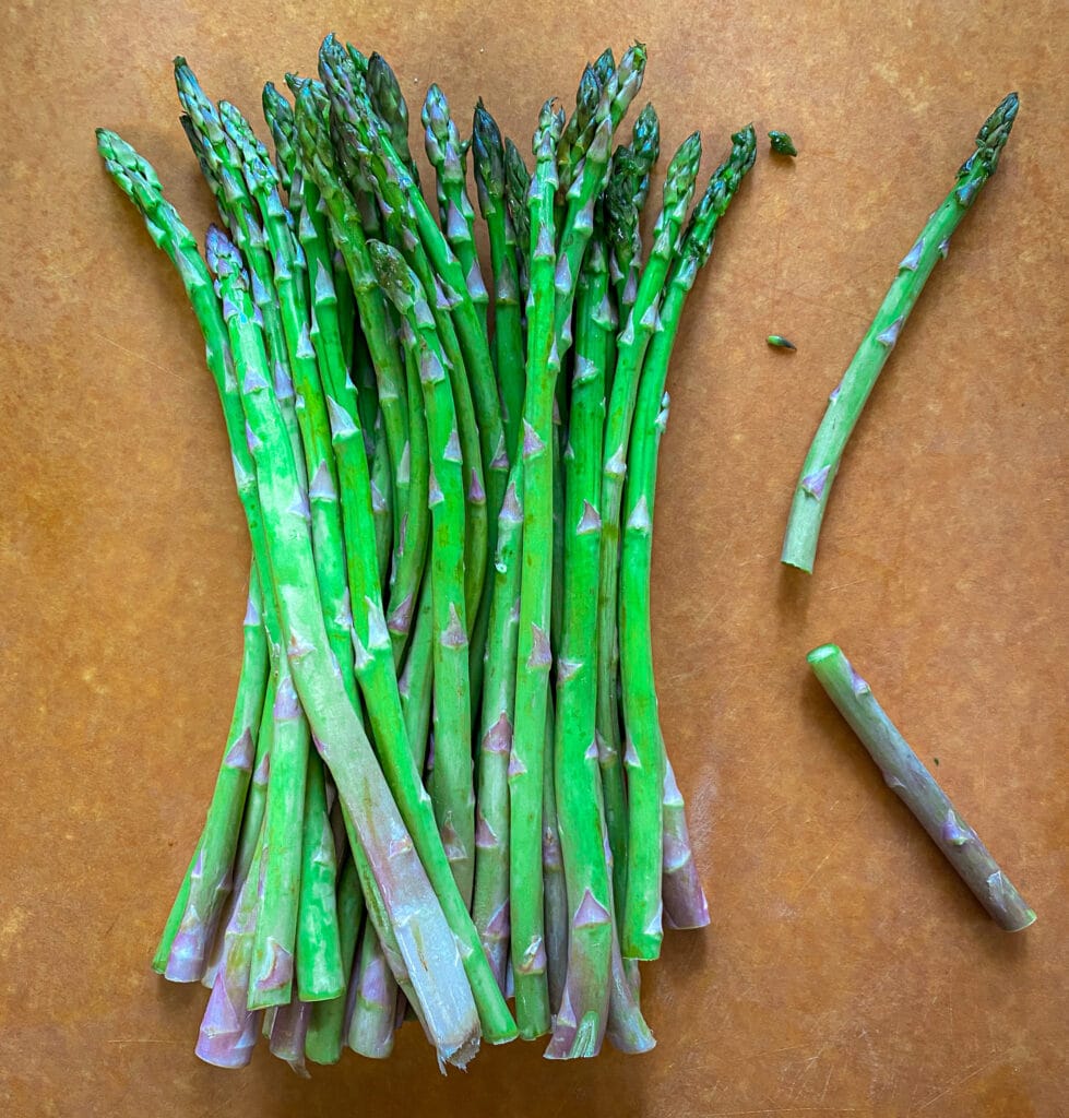 raw asparagus with one spear snapped next to the full bunch