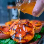 pouring sriracha honey glaze out of a small jar onto a grilled peach half