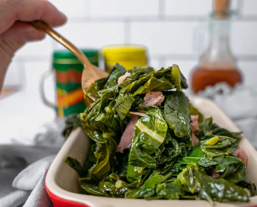 using a serving fork to scoop up southern collard greens with smoked turkey legs