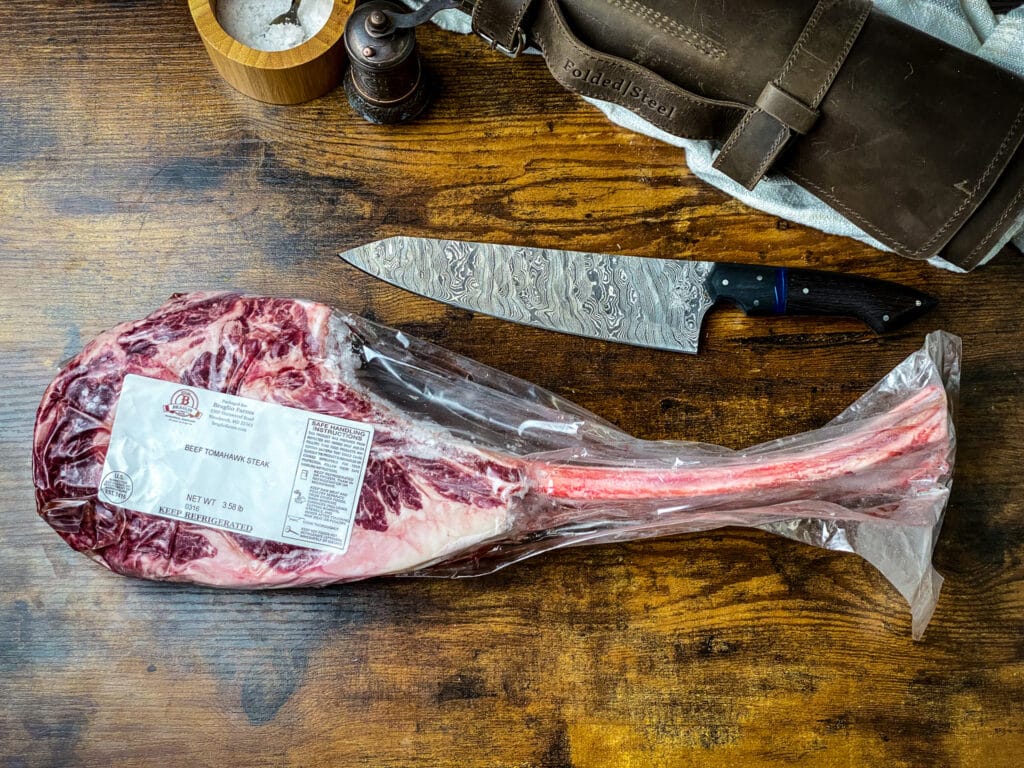 Raw tomahawk ribeye steak with Damascus steel chef knife