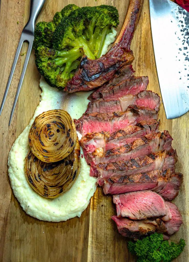 sliced tomahawk ribeye steak with mashed potatoes and grilled onions