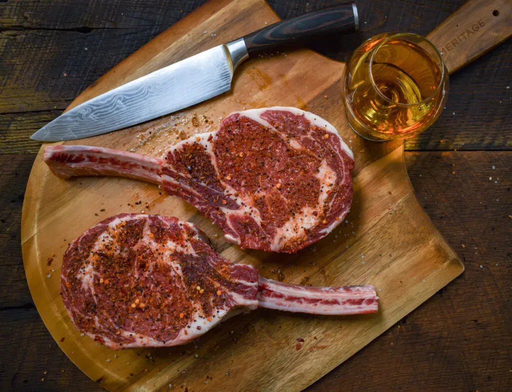 Cowboy ribeye steaks on a cutting board with a glass of bourbon