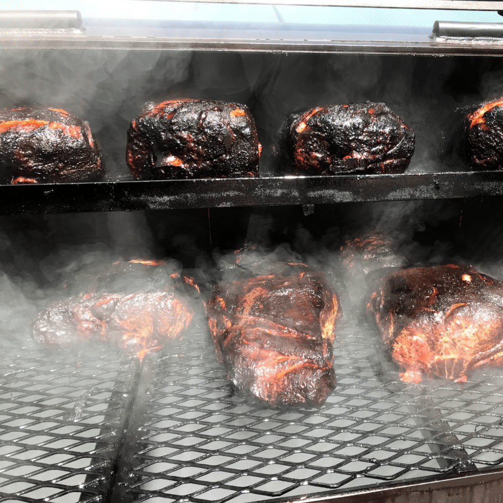 a bunch of pork butts on a smoker cooking