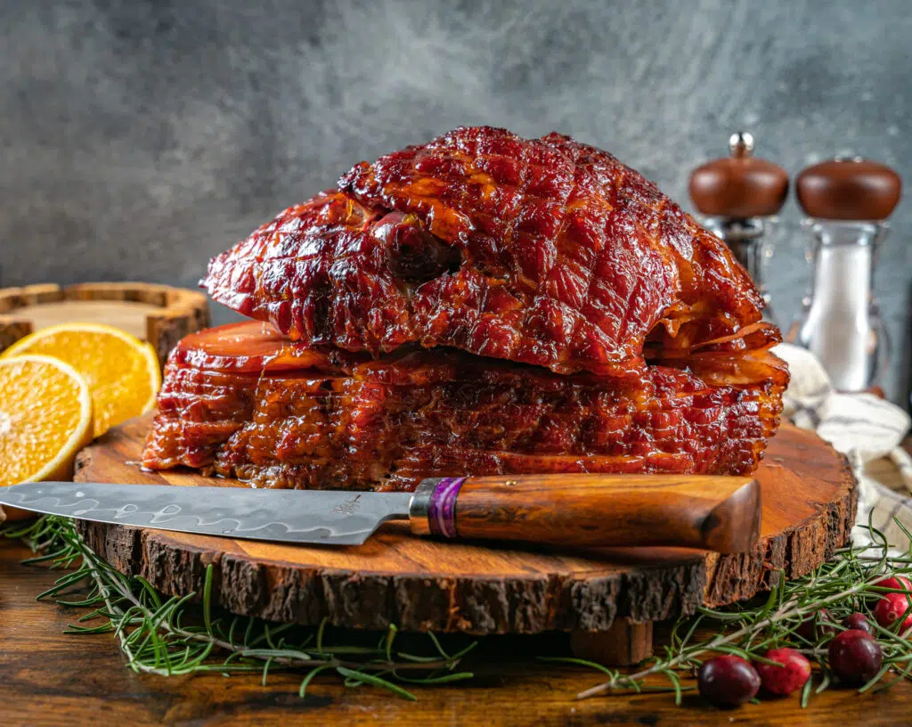 pellet grill ham with orange glaze on cutting board with knife and oranges in background 