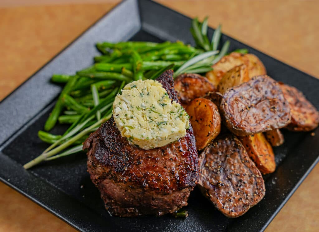 steak topped with blue cheese butter served with green beans and potatoes