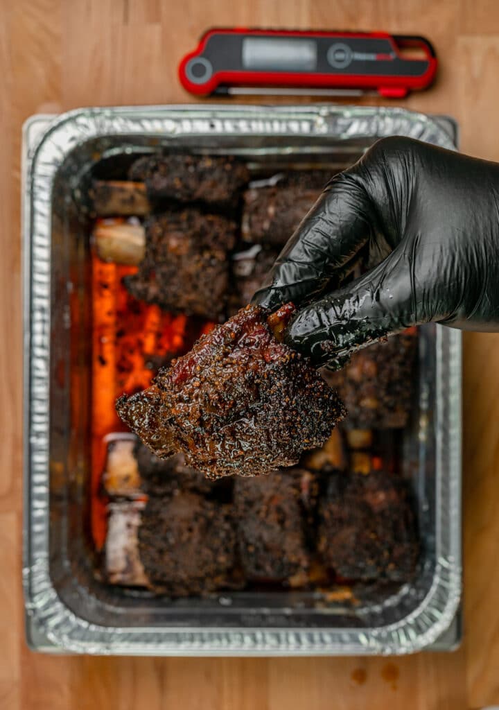 wearing a black glove to pick up smoked beef short ribs