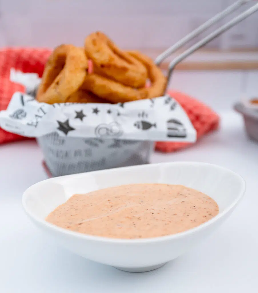 onion ring sauce in a white dish with a mini fry basket of onion rings in the background
