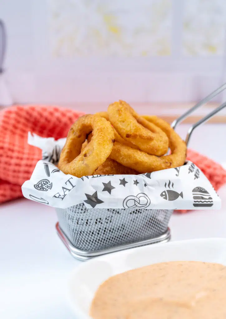 basket of onion rings with zesty sauce in a dish