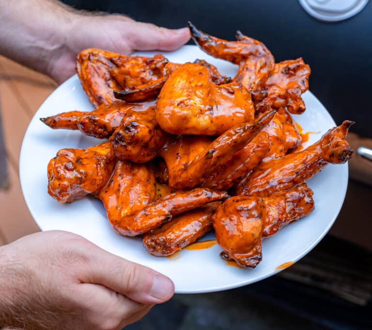 smoked chicken wings on a plat with a pellet grill in the background
