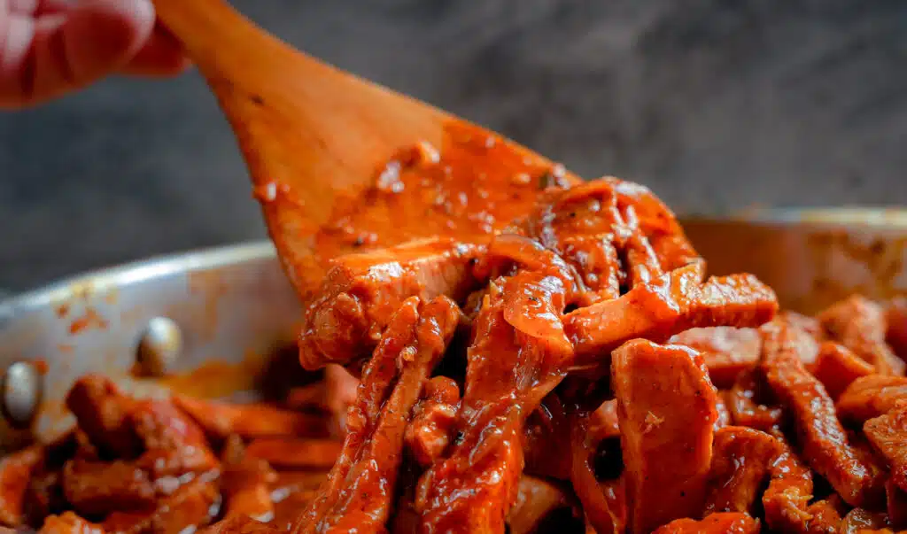 stirring pork carnitas simmering in sauce