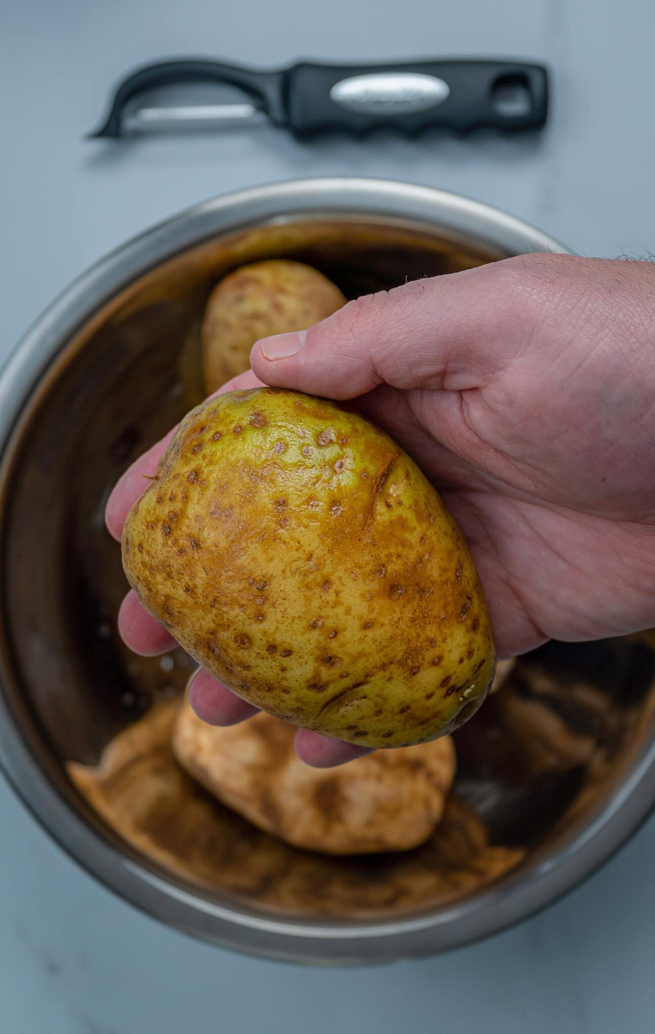 holding a russet potato over a bowl
