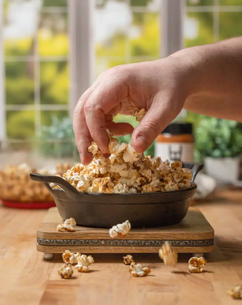 reaching hand into a skillet of smoked popcorn