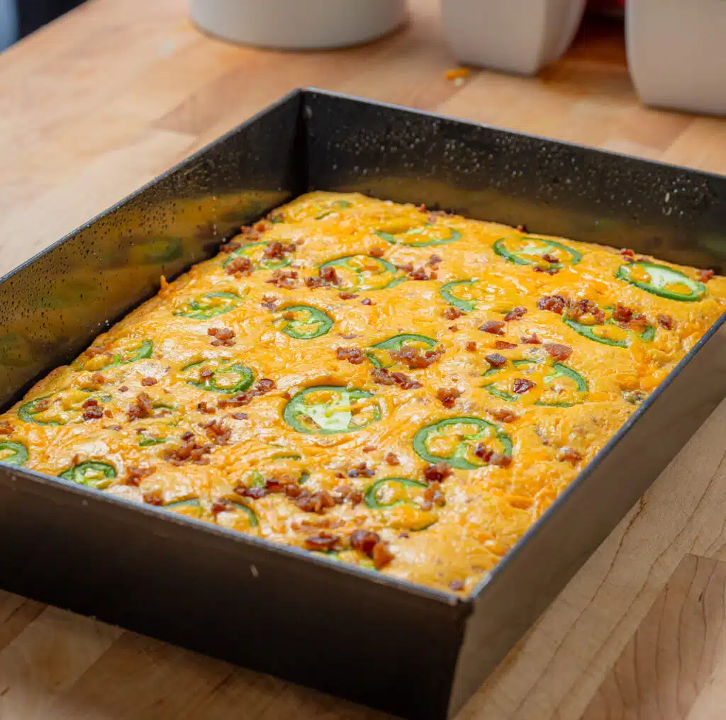 A pan of un cut cornbread topped with bacon and jalapeños 