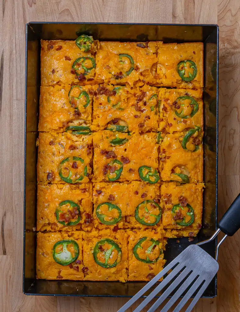 Cornbread in a pan cut into 18 squares topped with jalapeños and bacon