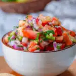 Fresh pico de Gallo in a white bowl with limes in the background