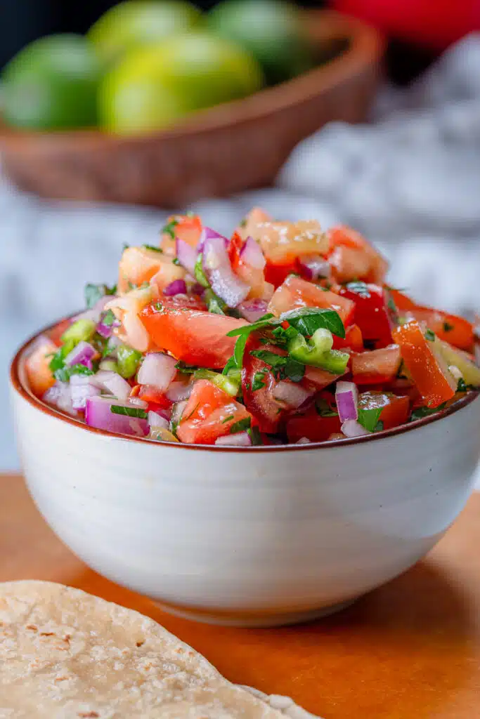 Fresh pico de Gallo in a white bowl with limes in the background