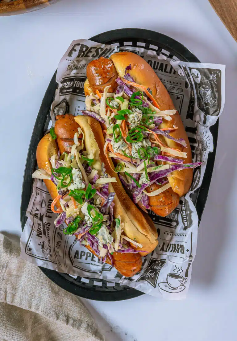bleu cheese coleslaw on top of 2 chicken sausage hot dogs in a basket with deli paper