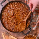 large cast iron skillet of smoked baked beans with a spoon