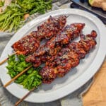 chicken on a stick glazed with teriyaki sauce on a plate with ginger and lime in the background