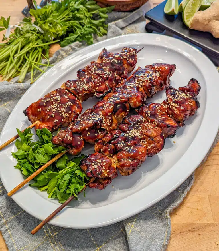 chicken on a stick glazed with teriyaki sauce on a plate with ginger and lime in the background
